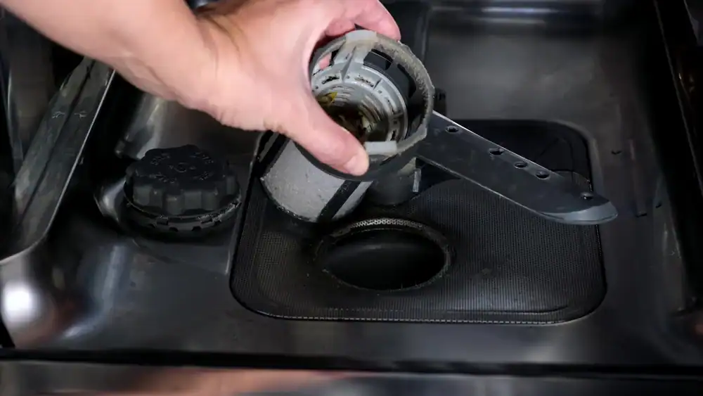 A hand lifts out the cylindrical filter from the bottom of a dishwasher for cleaning, revealing the drain and spray arm inside—just a simple step recommended by any professional plumber Brevard County, FL homeowners trust.