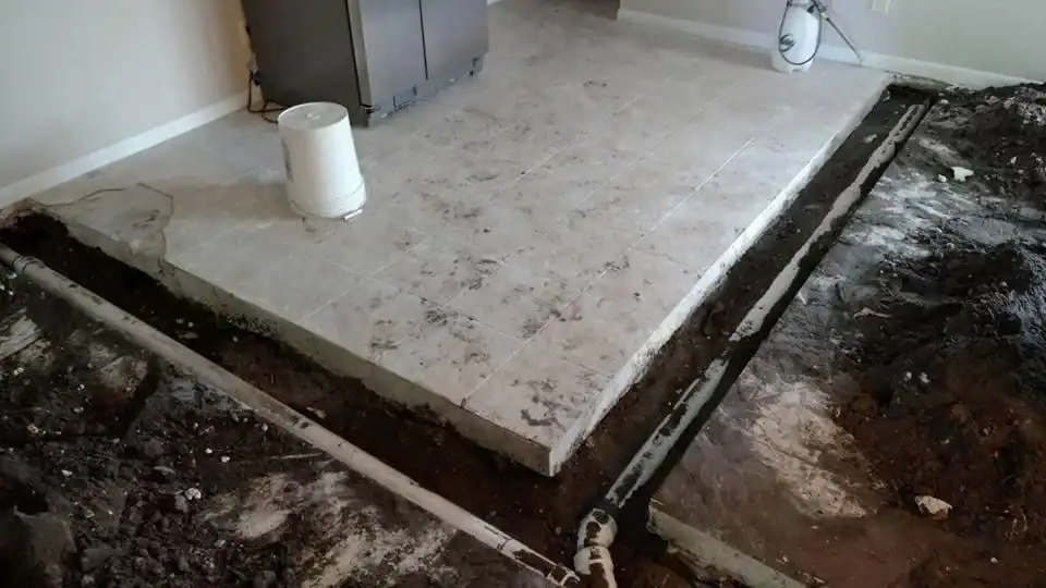 A kitchen area with tile flooring is elevated above an adjacent dirt floor. Exposed plumbing pipes and a trench run along the edge, hinting at ongoing work by a plumber Brevard County, FL. A white bucket sits on the tiles.