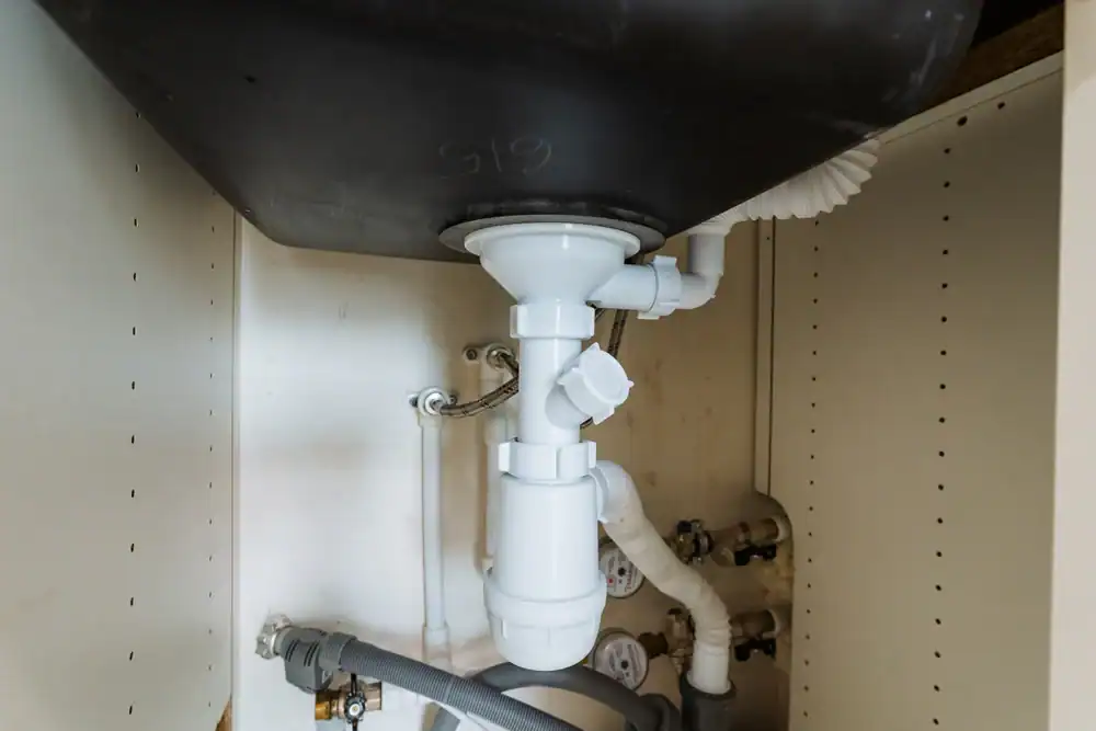 White PVC plumbing pipes and fittings under a sink inside an off-white cabinet, including a P-trap and supply and drainage connections. Professional installation by a plumber Brevard County, FL ensures secure, reliable plumbing for your home.