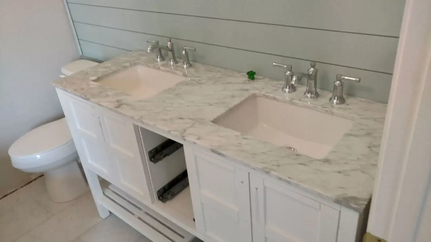 A bathroom with a double sink vanity featuring a marble countertop, two chrome faucets, an under-construction cabinet with open drawers, and a toilet to the left—expertly prepared by a plumber in Brevard County, FL.