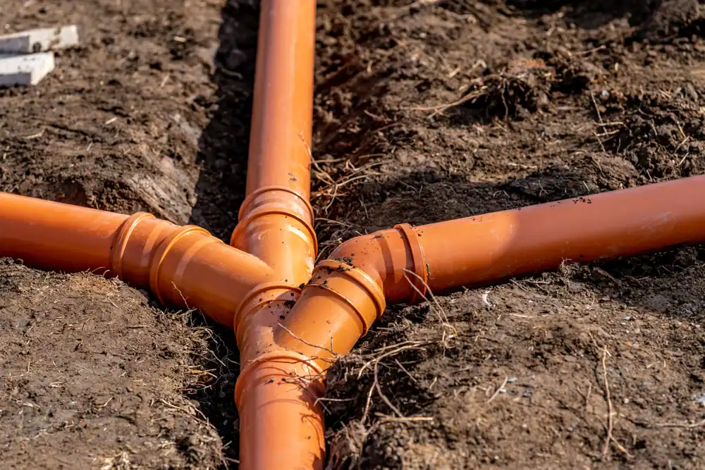 Orange plastic drainage pipes intersect underground in a dirt trench in FL, forming a connection point. The pipes are partly buried in soil, indicating ongoing construction or installation by a plumber Brevard County residents trust.