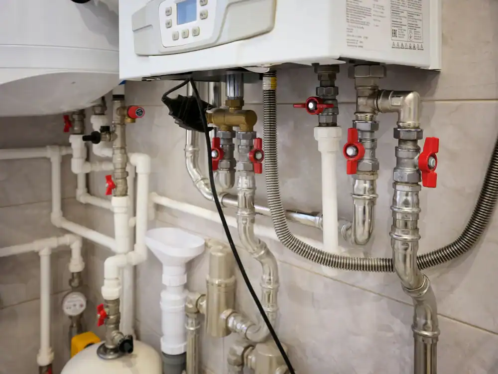 Close-up of a complex network of plumbing pipes, valves, and fittings connected to a white heating or boiler unit mounted on a tiled wall. Red handles and metal connections are visible, showcasing skilled work by a plumber Brevard County, FL.
