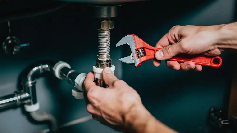 A plumber Brevard County uses a red adjustable wrench to tighten or loosen a pipe fitting under a sink, working on plumbing maintenance or repair in FL.