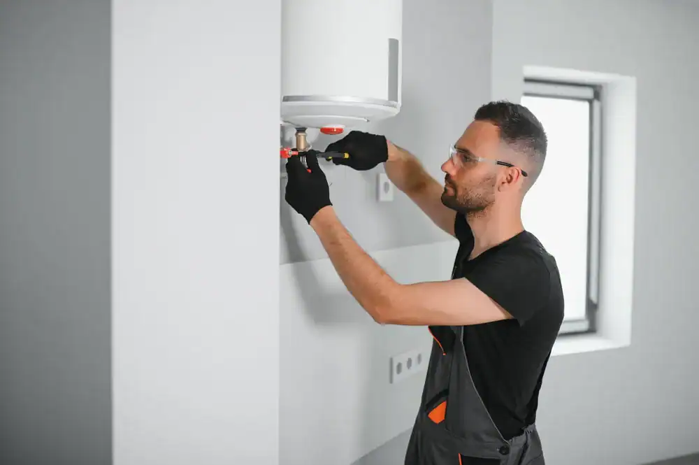 A plumber Brevard County, FL, wearing safety glasses and gloves, is fixing or installing a water heater on a wall inside a modern, bright room.