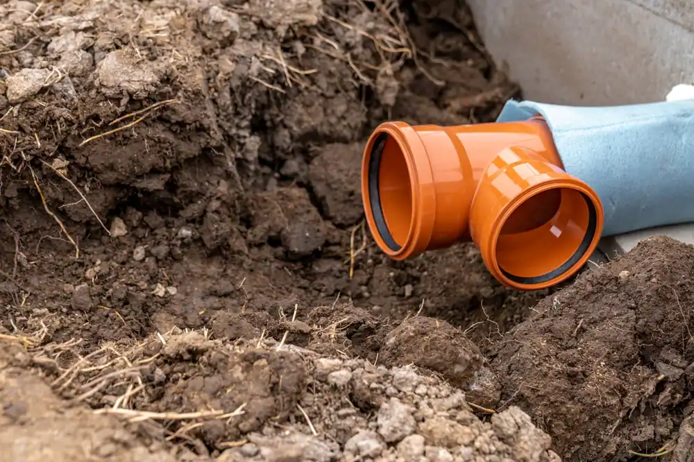Close-up of an orange PVC pipe T-joint partially buried in soil, with one end connected to a blue pipe—a typical scene for a plumber Brevard County, FL might encounter at a construction or plumbing site.